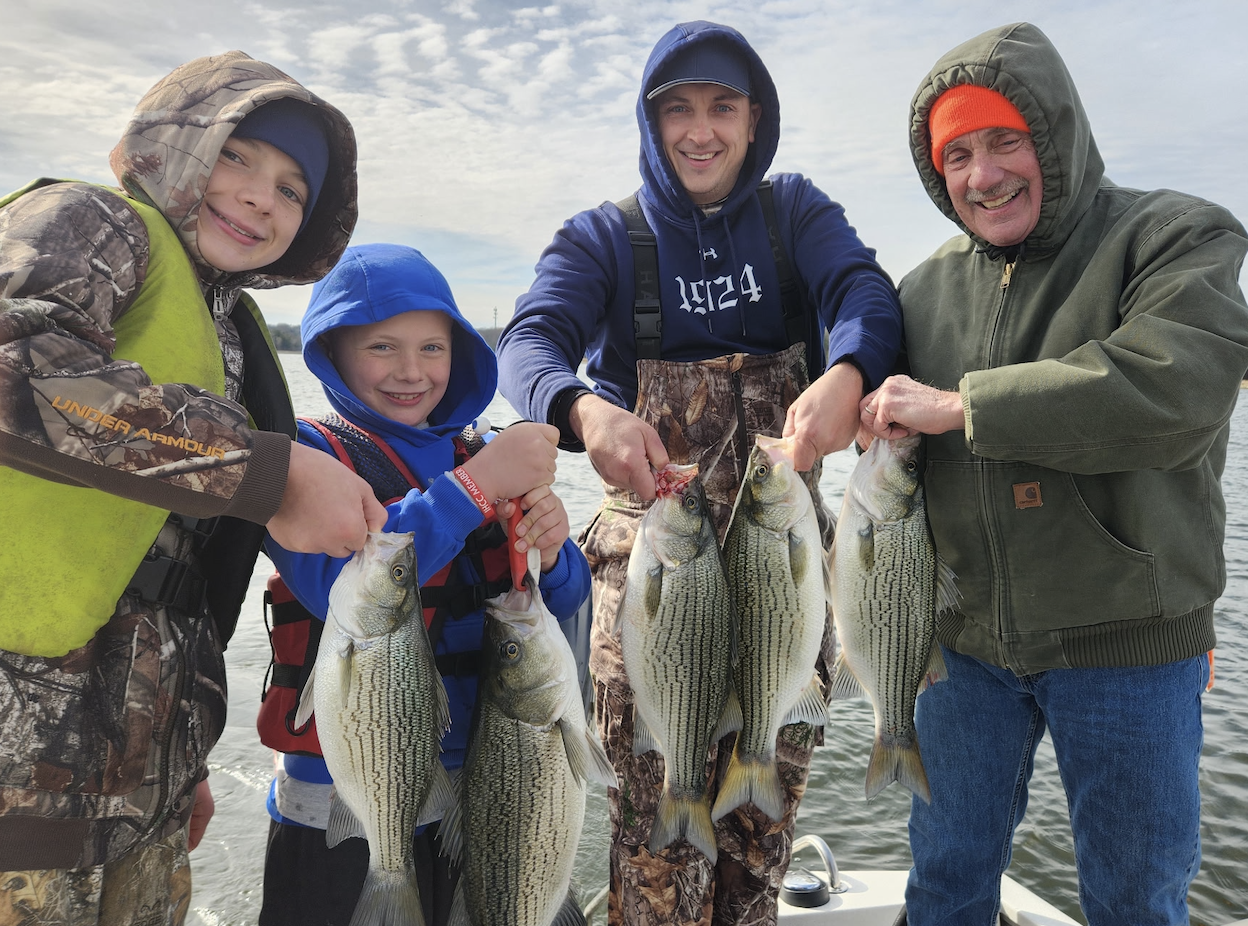Tommy, his sons, and his dad holding a line of striped bass on the lake